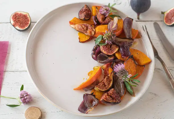 Homemade side dish with pumpkin, figs and red onions. Oven roasted and caramelized vegetable and fruit for autumn and winter season. Served on a white plate from above