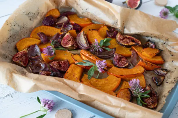 Oven roasted and caramelized vegetables and fruits such as hokkaido pumpkin, figs and red onions served on a baking sheet on white wooden table. Isolated and top view.