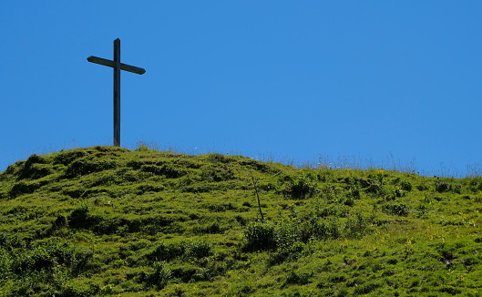grave hill with a cross with grass against a blue sky in austria