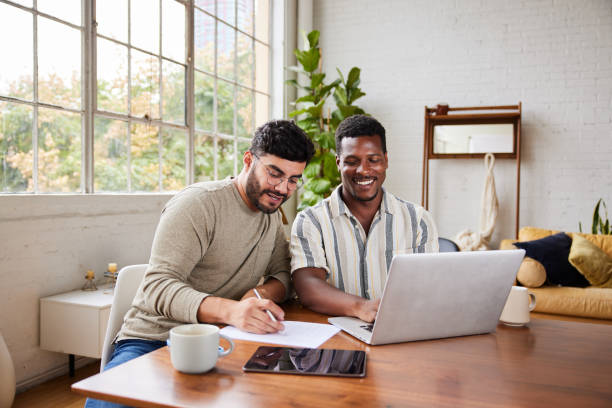 smiling young gay couple going over their home finances together - huishoudkosten stockfoto's en -beelden