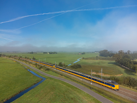 Intercity train of the Nederlandse Spoorwegen (NS) driving through the countryside landscape on the Hanzelijn in The Netherlands seen from above through the mist and clouds. The train is blurred caused by the speed its traveling.