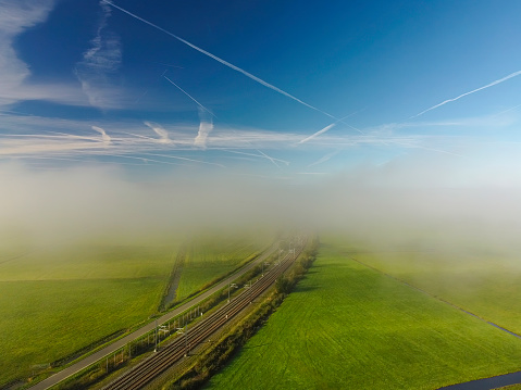 Railroad track Hanzelijn through the IJsseldelta countryside landscape in Overijssel, The Netherlands seen from above through the mist and clouds.