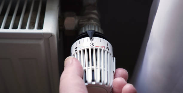 herunterdrehen des thermostats am heizkörper, um energie aufgrund der erhöhung der heizkostenpreise zu sparen - heizungsanlage stock-fotos und bilder