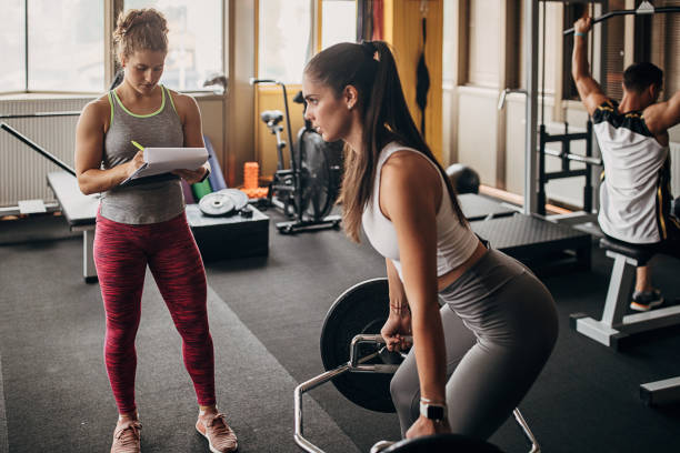 Fitness trainer watching a woman training Two people, woman exercises with weights while her female personal trainer is watching her in gym. fitness trainer stock pictures, royalty-free photos & images