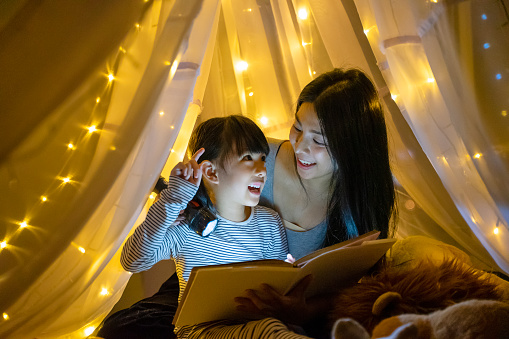 Mother read fairy tale for her daughter to listen at home. Leisure at home. Night scene with love and care.