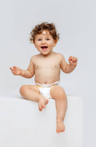 retrato vertical de un niño pequeño y lindo, un bebé en pañal sentado alegremente y riendo aislado sobre el fondo blanco del estudio. dulce infancia - baby cute laughing human face fotografías e imágenes de stock