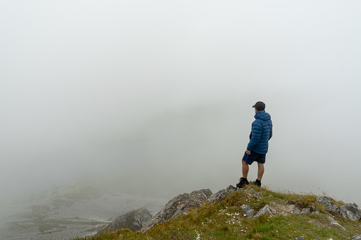 Man standing on top of mountain admiring landscape with fog