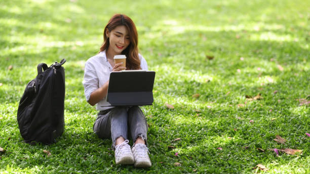 istock Beautiful asian woman drinking coffee and working with computer tablet in the park. 1346332622