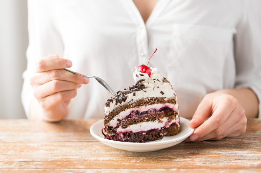 food, dessert and pastry concept - close up of woman eating piece of chocolate layer cake with maraschino cherry