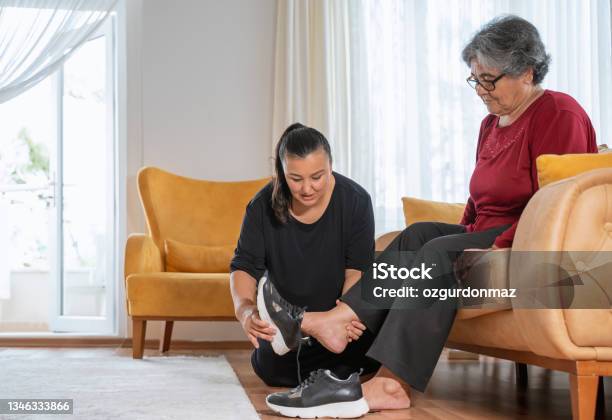 Woman Helping Her Elderly Mother In Wearing Shoes At Home Stock Photo - Download Image Now
