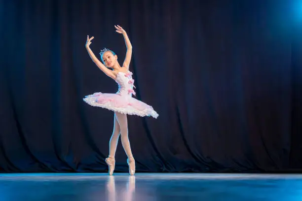 Photo of A little girl ballerina is dancing on stage in a white tutu on pointe shoes a classic variation.