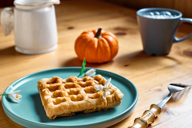 Healthy autumn breakfast. Pumpkin spice Belgian waffles with orange honey on light blue plate on wooden table. Autumn seasonal sweet food.