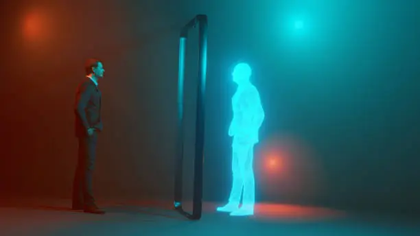 Concept image of man looking at his own digital twin mirrored through the frame of a mobile phone.  His twin is an avatar looking like a hologram.