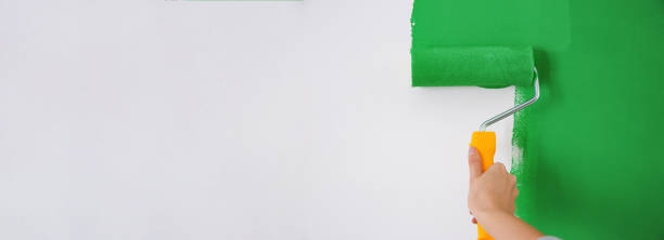 istock Professional decorator painting white wall with green dye, space for text. Banner design 1346338346