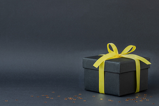 Holiday gift box with yellow ribbon on black background