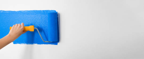 istock Professional decorator painting white wall with blue dye, space for text. Banner design 1346338475