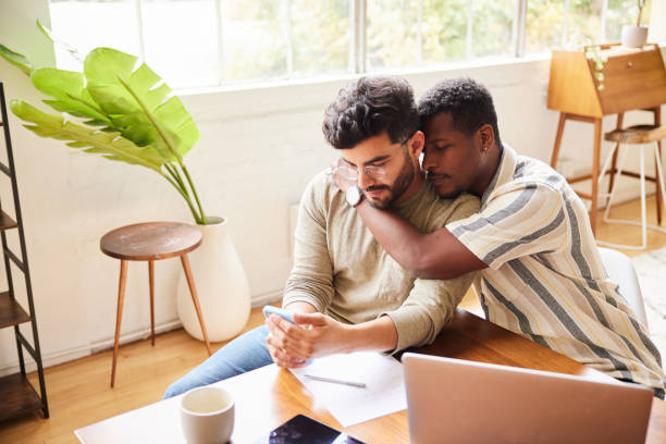 Gay couple doing their home finances using a smart phone and laptop stock photo