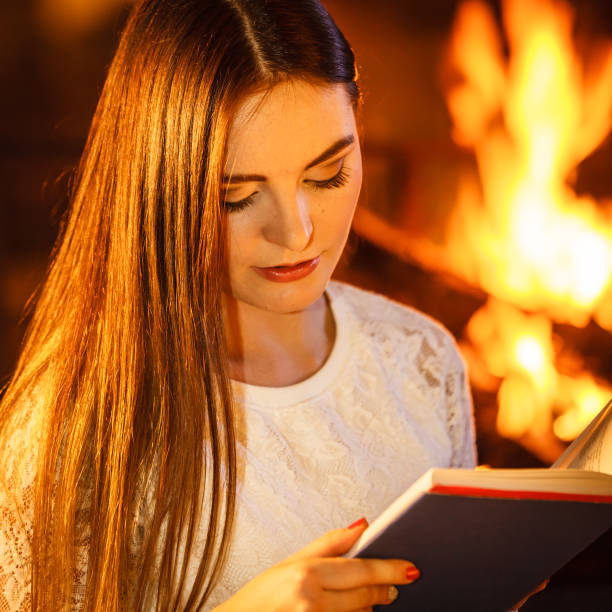 istock Woman reading book at fireplace. Winter home relax 1346340246