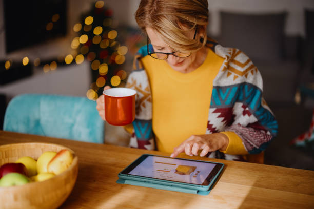 reife frau mit digitalem tablet für online-weihnachtseinkäufe - onlineshopping stock-fotos und bilder