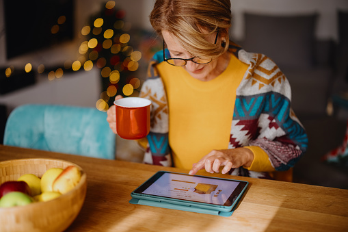 Mujer madura que usa la tableta digital para las compras navideñas en línea photo