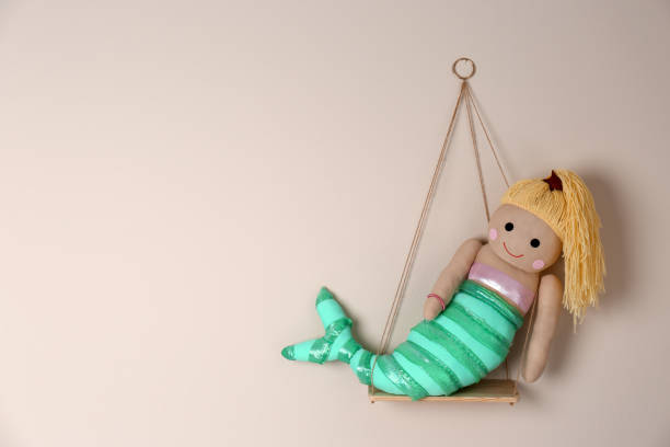 Shelf with cute toy mermaid on beige wall, space for text. Child's room interior element