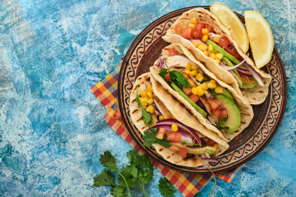 istock Mexican tacos with grilled chicken, avocado, corn kernels, tomato, onion, cilantro and salsa at blue stone table. Traditional Mexican and Latin american street food. Top view. 1346344119