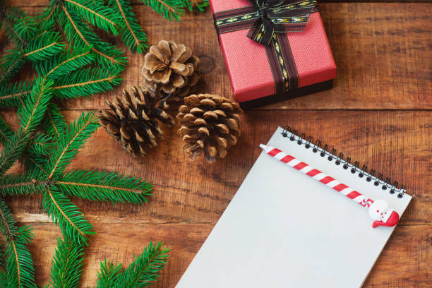 istock Christmas background. Spruce branches, gift, pinecones and notebook with pen on a wooden background 1346347102
