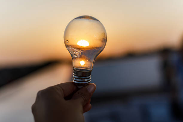 Close up of unrecognizable person holding light bulb at sunset.