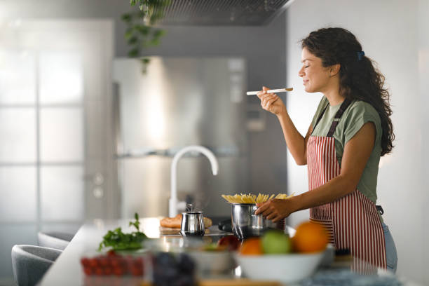 femme souriante appréciant tout en cuisinant des spaghettis pour le déjeuner. - cuisiner photos et images de collection