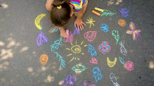 The child draws with chalk on the asphalt. Selective focus.