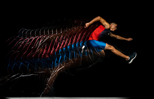Speed and strength. Young man, professional athlete jumping over the barrier isolated over black background. Stroboscope effect. Concept of sport, action, energy, health, movement. Copy space for ad