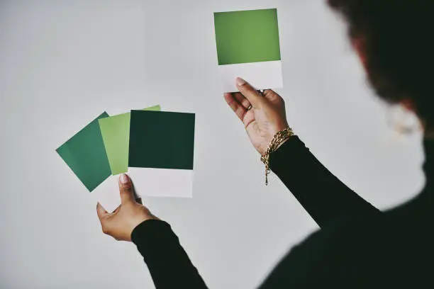 Photo of Cropped shot of an unrecognizable artist standing alone and holding up colour swatches in her studio