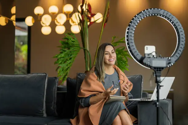 Photo of Beautiful woman performing a live from home while using her ring of light to illuminate herself and her cell phone to make the video