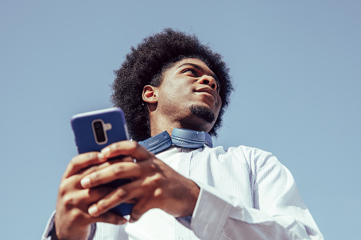 view from below of young african american man using smartphone