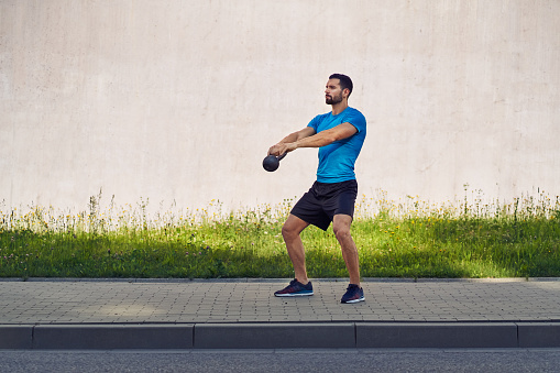 Athletic man exercising with kettlebell outdoors against concrete wall