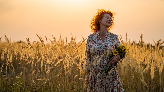 Senior red haired woman breathes fresh air in the fall in the field.