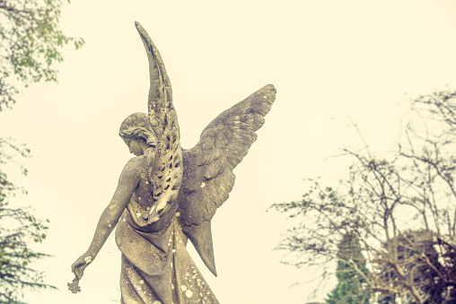 Angel seen from behind, guiding the soul to heaven. Sculpture in a cemetery. Spiritual peace. Melancholic and sad feelings.