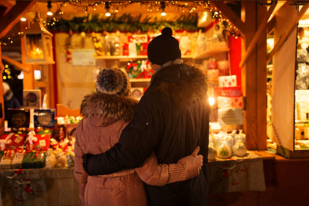 glückliches seniorenpaar umarmt sich auf dem weihnachtsmarkt - weihnachtsmarkt stock-fotos und bilder