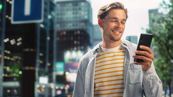 Portrait of a Handsome Young Man Wearing Casual Clothes and Using Smartphone on the Urban Street. Manager in Big City Connecting with People Online, Messaging and Browsing Internet.