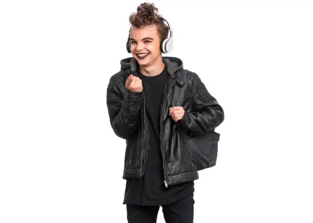 Portrait of teen boy student in headphones with spooking make-up holds bag, isolated on white background. Teenager with backpack in style of punk goth dressed in black. Problems of transitional age