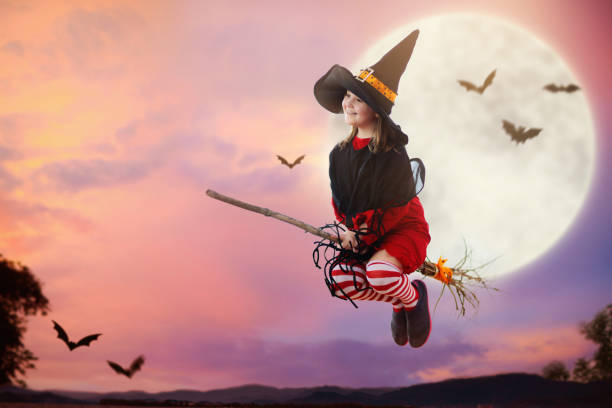 Little witch flying broom on Halloween night. Huge full moon and bats in the background. Kids trick or treat costume. Children have fun. Spooky and scary celebration. Kid dressed as evil ghost.