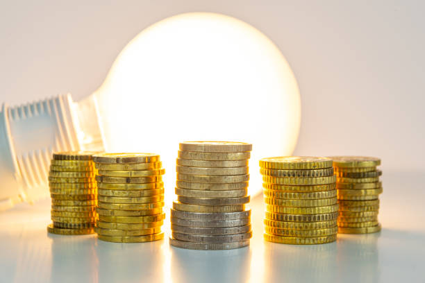 Lit light bulb with coins beside it. Energy tariffs increase. stock photo