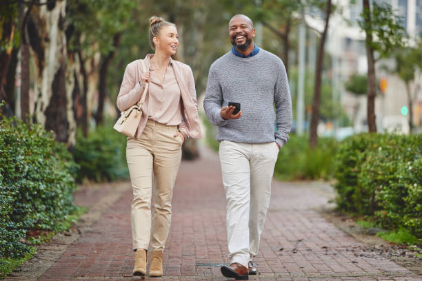 Full length shot of two corporate businesspeople chatting while walking through the city Headed to work black man blonde hair stock pictures, royalty-free photos & images