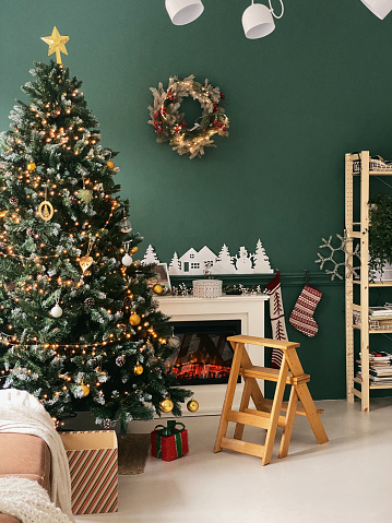 Interior of bright modern living room with fireplace, chandelier and comfortable sofa decorated with Christmas tree and red gifts. Vertical photo