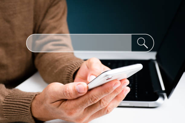 istock The man is on his phone while works on a laptop computer. With a blank search bar, the concept is Search engine Browsing Internet Data Information. Search Engine Optimization (SEO) Networking 1346371036