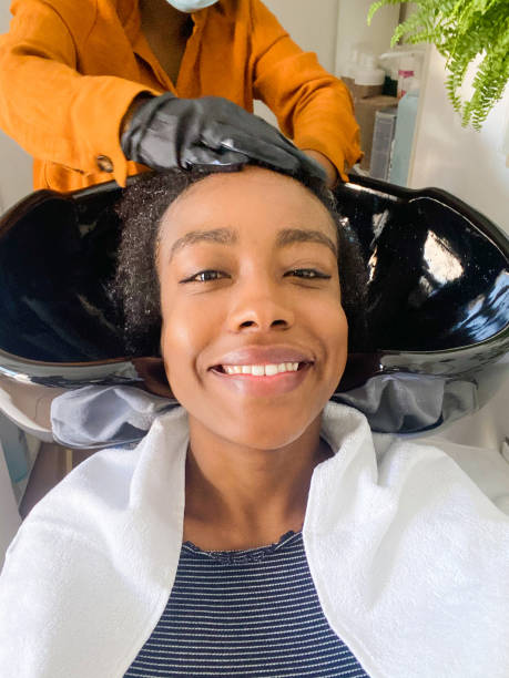 In a hair salon Photo of a smiling woman making a selfie while hairdresser washing her hair in a hair salon. black woman washing hair stock pictures, royalty-free photos & images
