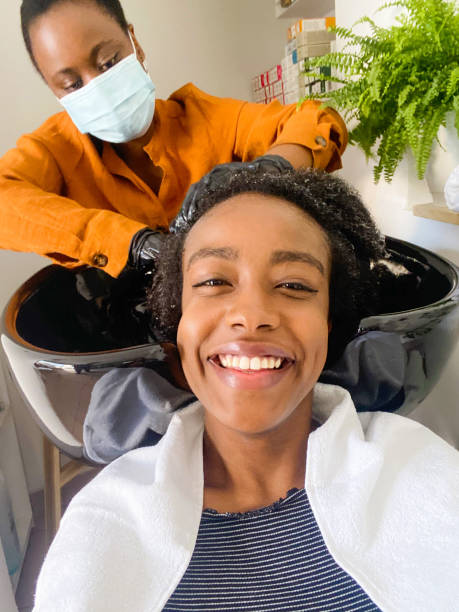 In a hair salon Photo of a smiling woman making a selfie while hairdresser washing her hair in a hair salon. black woman washing hair stock pictures, royalty-free photos & images