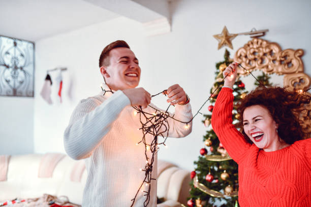 istock Smiling Male Laughing While Getting Tangle In Christmas Lights With Girlfriend 1346372387