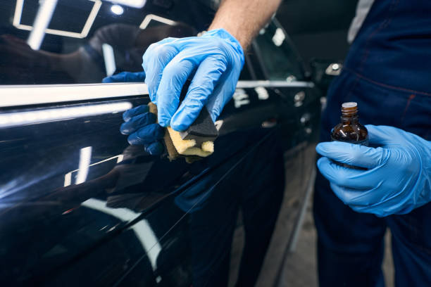 Worker with microfiber applicator spreading ceramic coating on car Hand in blue glove coating scratches on car surface with ceramic liquid from glass bottle ceramics stock pictures, royalty-free photos & images