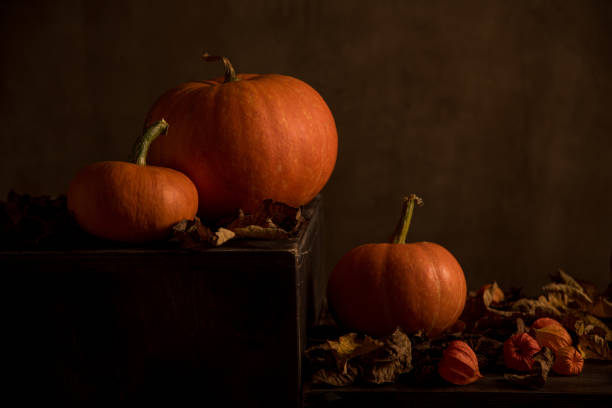 istock Orange pumpkins and dry leaves on dark background. 1346381691
